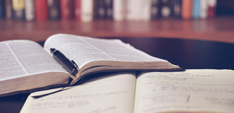 Notebook and reference book open on a table in front of a bookshelf