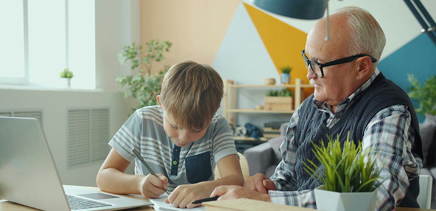 Older man sitting at a desk with a boy writing in a notebook
