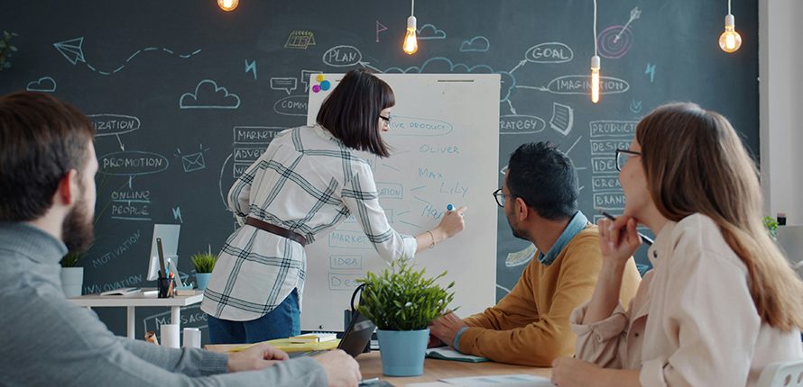 Group brainstorming, sitting at a desk while someone writes on a whiteboard